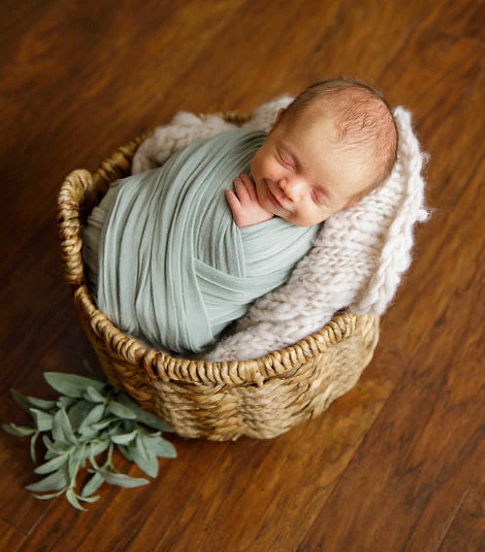 Reuben joined the competition — help win amazing prizes! baby, newborn, swaddled, basket, blanket, knitted_blanket, wicker_basket, wood_floor, hardwood, plant, leaves, smiling, sleeping, infant, portrait, studio, cozy, closeup, top_view, cute