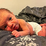 Reuben joined the competition — help win amazing prizes! baby, bed, bedding, blanket, cheek, closeup, curious_expression, diaper, eyes, face, fingers, gaze, hair, hand, infant, lying_down, newborn, patterned_bedspread, portrait, skin