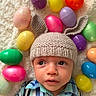 baby, child, knitted_hat, bunny_ears, easter_eggs, colorful, plastic_eggs, plaid_shirt, suspenders, blanket, soft_texture, portrait, indoors, cute, infant, headwear, holiday, spring, looking_away, laying_down