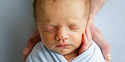 Reuben is registered to the contest to win money with this photo: baby, newborn, infant, swaddle, blanket, sleeping, hands, parent_hands, portrait, closeup, face, head, hair, eyes_closed, soft_light, studio, calm, pale_background, skin, peaceful