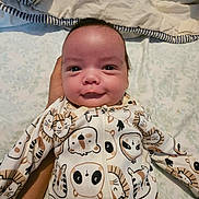 Ramey is registered to the contest to win money with this photo: baby, infant, onesie, animal_print, smile, hand, bed, blanket, sleepwear, cute, lying_down, child, newborn, face, person, soft_lighting, indoor, comfort, toddler, patterned_fabric