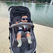 Ramey joined the competition — help win amazing prizes! baby, child, stroller, sunglasses, lakeside, lake, fountain, outdoor, park, water, autumn, trees, houses, sidewalk, infant, seated, portrait, socks, gray_stroller, daylight