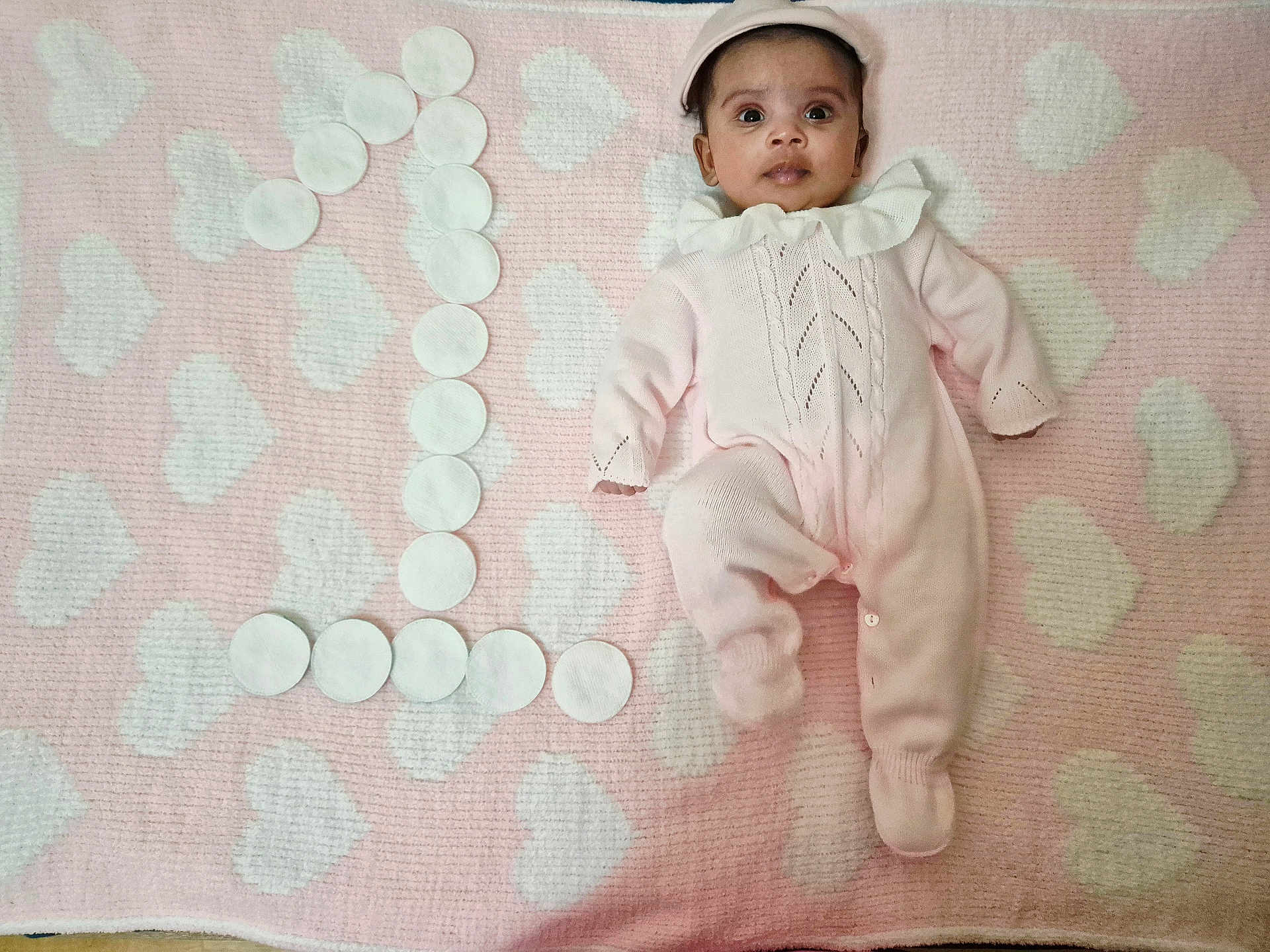 Athithi is registered to the contest to win money with this photo: baby, infant, pink_outfit, blanket, heart_pattern, cotton_pads, number_one, lying_down, cute, soft_texture, child, portrait, celebration, milestone, headwear, face, small_person, indoors, cozy, one_year