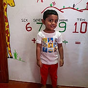 Aarvish joined the competition — help win amazing prizes! child, boy, barefoot, red_pants, white_tshirt, cartoon_characters, giraffe_mural, numbers, educational_wall, indoor, smiling, short_hair, wall_art, colorful, floor, standing, young_child, playful, learning, happy