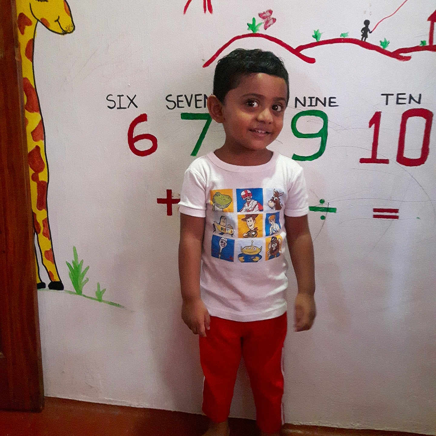 Aarvish joined the competition — help win amazing prizes! barefoot, boy, cartoon_characters, child, colorful, educational_wall, floor, giraffe_mural, happy, indoor, learning, numbers, playful, red_pants, short_hair, smiling, standing, wall_art, white_tshirt, young_child