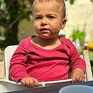 Marie-Lou a rejoint le concours — aidez-le/la à gagner de superbes lots ! toddler, child, red_shirt, high_chair, outdoor, daylight, face, expression, hands, table, cup, garden, blurred_background, person, portrait, seated, casual_clothing, young_child, natural_light, curious