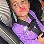 child, girl, car_seat, curly_hair, hair_bow, purple_shirt, seatbelt, car_interior, puckered_lips, funny_face, safety, cute, young_child, portrait, seat, buckled_up, car, expression, casual_clothing, indoor