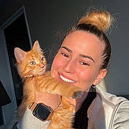 Nahya participe au concours pour gagner de l'argent avec cette photo : casual_clothing, cat, closeup, cozy, cute, domestic_animal, feline, friendly, hair_bun, happy, holding, indoor, orange_tabby, person, pet, portrait, smile, sunlight, warm_light, watch