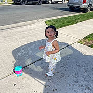 Lailah is registered to the contest to win money with this photo: toddler, child, girl, sidewalk, bubble_machine, bubbles, outdoor, sunny, residential_area, plants, grass, vehicles, car, pickup_truck, black_suv, concrete, shadow, summer_clothing, pigtails, playtime