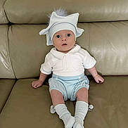 Reaves is registered to the contest to win money with this photo: baby, infant, hat, white_clothing, blue_clothing, socks, couch, leather, sitting, wide_eyes, cute, adorable, child, indoor, portrait, expression, pom_pom, casual, furniture, young