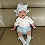 baby, infant, hat, white_clothing, blue_clothing, socks, couch, leather, sitting, wide_eyes, cute, adorable, child, indoor, portrait, expression, pom_pom, casual, furniture, young