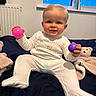 Harland is registered to the contest to win money with this photo: baby, bed, blanket, child, cozy, cute, face, happy, indoor, onesie, person, pink_ball, purple_ball, room, sitting, smiling, soft_toy, teddy_bear, toy, window