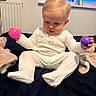 Harland is registered to the contest to win money with this photo: baby, bed, blanket, child, clothing, cute, face, hands, home, indoor, infant, pajamas, person, pink_ball, purple_ball, radiator, sitting, soft_toys, toy, window