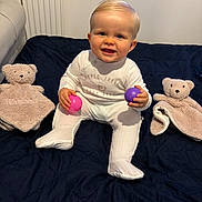 Harland is registered to the contest to win money with this photo: baby, ball, bedspread, blanket, child, cute, furniture, happy, indoors, infant, onesie, person, quilt, radiator, sitting, smiling, soft_toy, teddy_bear, toy, window