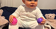 Harland joined the competition — help win amazing prizes! baby, bed, blanket, blue_window, child, curious, cute, happy, home, indoor, infant, onesie, person, pink_ball, portrait, purple_ball, sitting, soft_toy, teddy_bear_blanket, white_clothing