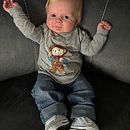 Harland joined the competition — help win amazing prizes! baby, blue_eyes, casual, child, clothing, couch, cute, footwear, furniture, gray_sweatshirt, indoor, jeans, light_hair, person, playful, sitting, smiling, teddy_bear_graphic, white_sneakers, young_child