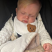 Harland is registered to the contest to win money with this photo: baby, sleeping, blanket, knitwear, bib, teddy_bear_patch, pacifier, hand, face, cozy, child, infant, soft_texture, warm_clothing, car_seat, portrait, indoor, peaceful, cute, resting