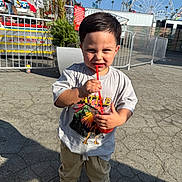 Gerardo is registered to the contest to win money with this photo: child, boy, drink, straw, tshirt, sneakers, carnival, ferris_wheel, sunny, outdoor, pavement, fence, plant, smiling, daytime, amusement_park, casual_clothing, fun, portrait, young