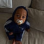 baby, casual, child, clothing, comfort, couch, curious, cute, expression, face, foot, home, hoodie, indoor, pacifier, person, relaxed, sitting, tracksuit, young