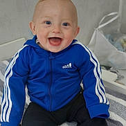 Eddy participe au concours pour gagner de l'argent avec cette photo : baby, child, smiling, blue_jacket, adidas, sitting, indoor, towel, striped, happy, face, clothing, socks, pants, person, cute, young, infant, portrait, casual