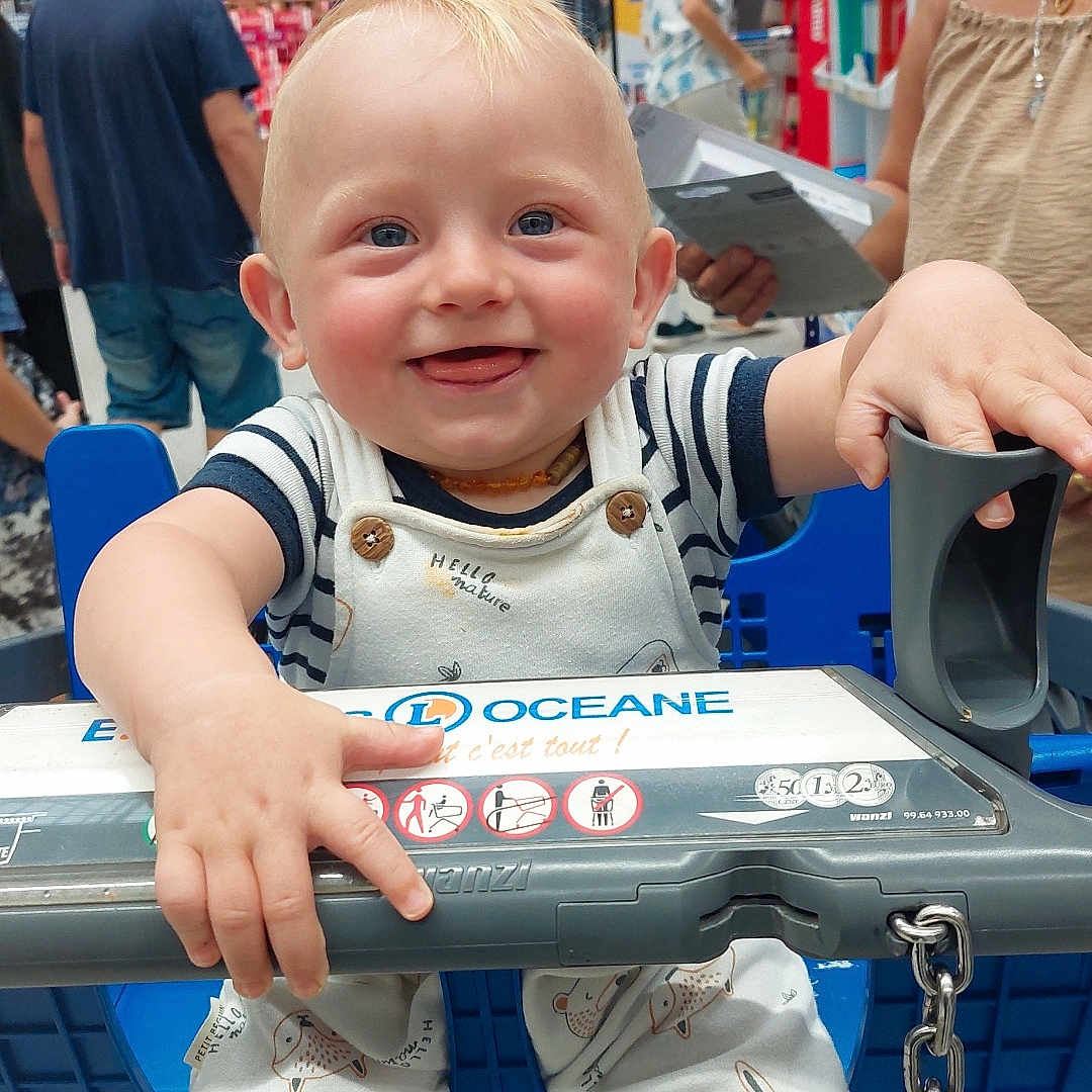 Eddy participe au concours pour gagner de l'argent avec cette photo : adult, aisle, baby, blue_eyes, bunny_print, chain, child, clothing, hand, happy, indoor, overalls, parent, person, retail, shopping, shopping_cart, smiling, socks, supermarket