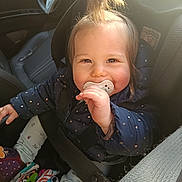 Lou a rejoint le concours — aidez-le/la à gagner de superbes lots ! child, baby, toddler, pacifier, car_seat, seatbelt, tuft_hair, smiling, cheeks, winter_jacket, polka_dot, toy, colorful_toys, leg_warmers, car_interior, steering_wheel, portrait, sunlight, happy, close_up