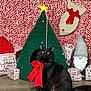 Phoebe joined the competition — help win amazing prizes! black_cat, cat, red_bow, christmas_tree_house, gift_boxes, gnome, holiday_decor, festive, yellow_eyes, wooden_floor, red_background, plush, indoor, pet, decorations, christmas, cozy, celebration, feline, animal