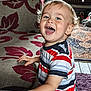 Elijah Blue is registered to the contest to win money with this photo: blue_eyes, carpet, child, couch, curly_hair, cute, fabric, furniture, hand, happy, home, indoor, laughing, living_room, pattern, person, portrait, smiling, striped_shirt, toddler
