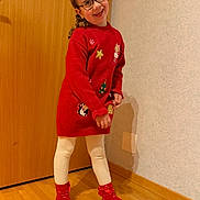 Sarah participe au concours pour gagner de l'argent avec cette photo : bows, child, curly_hair, floor, footwear, girl, glasses, happy, holiday_theme, indoor, long_hair, person, posing, red_socks, red_sweater, smiling, tights, wall, wooden_door, wooden_floor