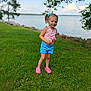 Drailee joined the competition — help win amazing prizes! child, girl, grass, lake, water, blue_shorts, pink_top, pigtails, outdoor, summer, nature, smile, playing, greenery, footwear, pink_shoes, sky, trees, rocks, portrait