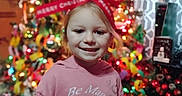 Drailee joined the competition — help win amazing prizes! celebration, child, christmas_lights, christmas_tree, colorful, decorations, face, festive, happy, holiday, indoors, person, pink_hoodie, portrait, red_bow, seasonal, smile, smiley_face, smiling, young_child