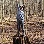 child, hoodie, sweatpants, tree_stump, forest, leaf_litter, peace_sign, outdoor, nature, sunlight, trees, standing, casual_clothing, young_person, autumn, bare_trees, calm, daytime, woodland, pose