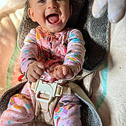 Ophelia is registered to the contest to win money with this photo: baby, child, smiling, happy, pajamas, colorful_clothing, cushion, seat, harness, baby_seat, infant, playful, indoor, face, hands, feet, closeup, joy, cute, messy