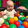 baby, child, ball_pit, colorful_balls, play_area, indoor, padded_walls, smiling, happy, fun, toys, playtime, infant, cute, person, head, face, clothing, early_childhood, recreation