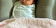 Leilia is registered to the contest to win money with this photo: baby, newborn, swaddled, blanket, cushion, sleeping, infant, soft_texture, pink, white, face, head, resting, cozy, indoors, person, peaceful, wrapped, young_child, child