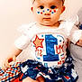 Serenity is registered to the contest to win money with this photo: baby, child, face_paint, blue_bow, white_shirt, skirt, sitting, indoor, portrait, cute, red_white_blue, patterned_clothing, infant, headband, legs, blanket, celebration, holiday, smile, person