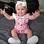 baby, child, infant, smiling, pink_clothing, headband, white_shoes, arms_outstretched, sitting, bed, indoor, cute, happy, person, face, room, car_seat, blanket, footwear, domestic