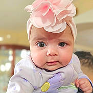 Melania is registered to the contest to win money with this photo: baby, infant, face, headband, flower, clothing, purple, pink, person, child, cute, closeup, portrait, indoor, soft_light, curious, holding, shoulder, young, adorable