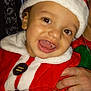 child, toddler, santa_hat, santa_outfit, smiling, holiday, festive_clothing, indoor, person, celebration, happy, cute, christmas, red, white, face, hand, costume, joy, festivity