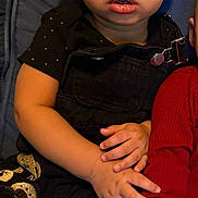 D'Angelo joined the competition — help win amazing prizes! baby, black_clothing, blue_cushion, casual, child, closeup, couch, curious, curly_hair, expression, gold_accents, hand_holding, headband, indoor, overalls, person, portrait, red_sleeve, sitting, toddler