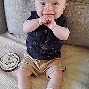 Loan participe au concours pour gagner de l'argent avec cette photo : baby, infant, smiling, couch, clothing, shorts, shirt, shoes, socks, milestone, wooden_marker, indoor, person, face, happy, seated, child, cute, hands, blue_eyes