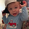 toddler, child, cap, backward_cap, blue_shirt, red_truck, couch, floral_pattern, indoor, smiling, happy, playful, person, home, casual_clothing, young_child, sitting, portrait, cute, fun