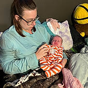 Paisley is registered to the contest to win money with this photo: newborn, baby, infant, adult, parent, caregiver, holding, cradling, sleepy, face, portrait, striped_outfit, orange_clothing, glasses, blankets, pillows, bed, indoors, stuffed_toy, family