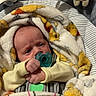 baby, infant, child, newborn, pacifier, blanket, plush_toy, stuffed_animal, car_seat, cushion, sleepy, awake, face, hands, portrait, indoors, cozy, textile, yellow_clothing, seated