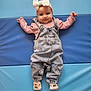 baby, child, infant, denim_overalls, pink_shirt, headband, bow, socks, animal_socks, blue_background, padded_surface, smiling, happy, cute, portrait, lying_down, indoors, clothing, person, young_child