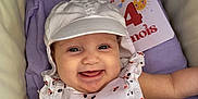 Maëlle a rejoint le concours — aidez-le/la à gagner de superbes lots ! baby, infant, smiling, white_cap, floral_dress, blanket, purple, milestone_card, 4_months, happy, cute, lying_down, child, person, face, hand, indoors, soft_lighting, portrait, close_up