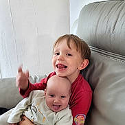 Maëlle participe au concours pour gagner de l'argent avec cette photo : baby, child, couch, cozy, cute, face, happy, hug, indoor, infant, living_room, person, playful, red_shirt, seated, sibling, smile, toddler, tongue_out, white_onesie