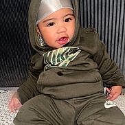 Zuuneil is registered to the contest to win money with this photo: baby, child, portrait, sitting, hood, headband, tracksuit, olive_clothing, fashion, serious_expression, face, eyes, lips, indoors, striped_background, textile, cushion, infant, photography, nike_logo