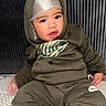 baby, child, portrait, sitting, hood, headband, tracksuit, olive_clothing, fashion, serious_expression, face, eyes, lips, indoors, striped_background, textile, cushion, infant, photography, nike_logo