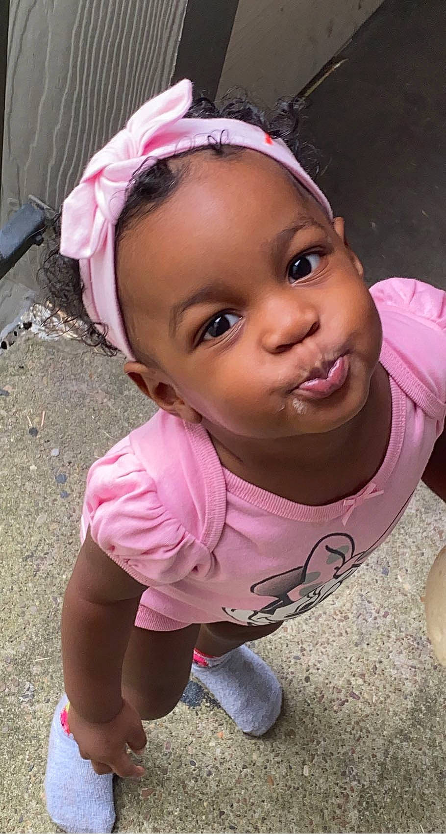 Delilah is registered to the contest to win money with this photo: baby_toddler_clothing, black_hair, cheek, chin, clothing, dress, eyelash, fun, grass, happy, headgear, lip, magenta, mouth, nose, person, pink, purple, skin, toddler